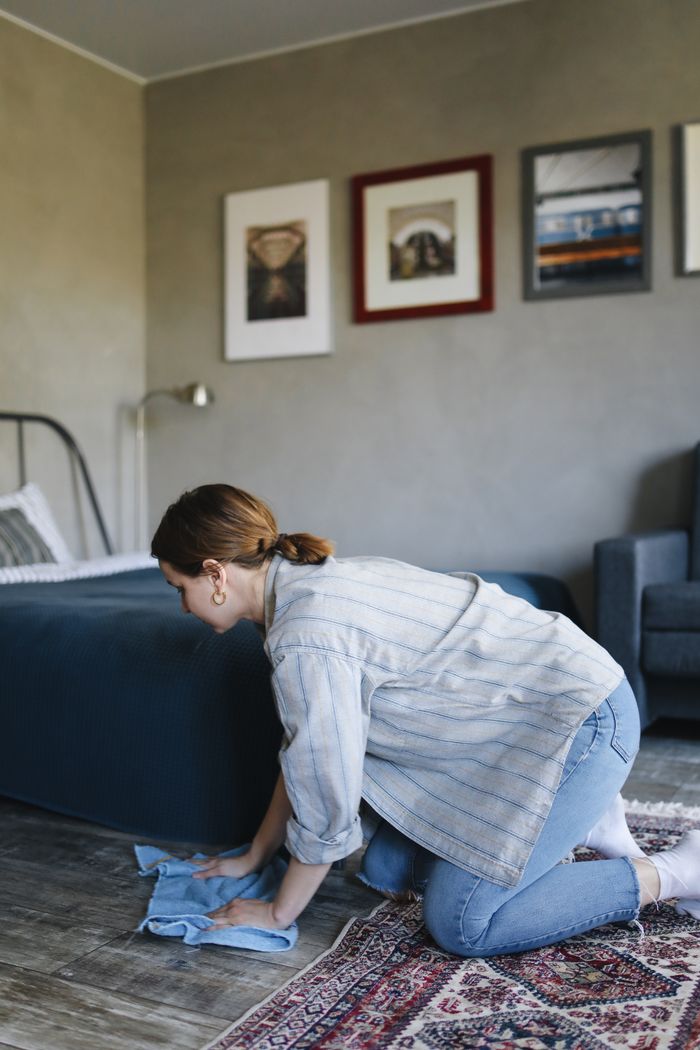 A woman cleaning the floor in a cozy bedroom using a cloth on a carpet.